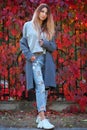 Dreamy beautiful girl with long colorful hair on autumn background of red grape hedge. Inspired woman in gray coat. Autumn Royalty Free Stock Photo