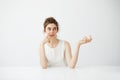 Dreamy beautiful young girl with bun sitting at table over white background thinking dreaming. Royalty Free Stock Photo