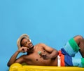 Dreamy black man sunbathing on inflatable lilo, drinking tropical cocktail from coconut shell on blue background Royalty Free Stock Photo
