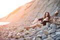 Dreamy lonely brunette hippie in the style of bokho chic sits on gray stones at the sea shore in the rays of the setting sun