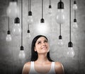 A dreamy brunette looks upward. Lots of light bulbs, one of them is turned on.