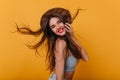 Dreamy caucasian girl with long hairstyle happy dancing in studio with bright interior. Pretty laughing lady in hat and