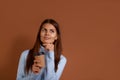 Dreamy caucasian woman wearing light blue sweater holds her index finger under chin and a paper cup of hot coffee, drinks takeaway Royalty Free Stock Photo
