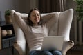 Dreamy cheerful millennial girl using laptop on lap