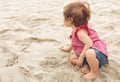 Dreamy child. Cute dark-haired kid tiny little child baby girl sitting on haunches and playing with sand on beach on Royalty Free Stock Photo