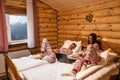 Teen friends in same Christmas pajamas relaxing in bed inside cozy log cabin with winter view Royalty Free Stock Photo