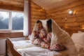 Teen friends in same Christmas pajamas relaxing in bed inside cozy log cabin with winter view Royalty Free Stock Photo