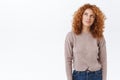 Dreamy, creative good-looking redhead curly girl in blouse, jeans, looking up thoughtful, smiling devious, picturing