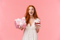 Dreamy, fascinated and wishful cute b-day girl with red curly hair in white dress celebrating birthday, holding wrapped