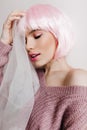 Dreamy girl with bright makeup posing on light background in pink periwig with eyes closed. Studio shot of shy pretty