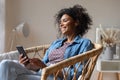 Dreamy happy African American woman holding smartphone, looking in distance Royalty Free Stock Photo