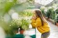 Dreamy kid spending time in orangery. Positive little girl in yellow sweater looking at green plants Royalty Free Stock Photo