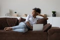 Dreamy millennial african woman resting on couch with computer.