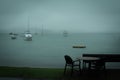 Dreamy photo of an empty seaside cafe table on a raint day. Small leasure boats anchored near the coast of Russel, New