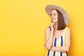 Dreamy positive optimistic woman wearing striped swimming suit and hat isolated on yellow background looking away with smile copy