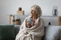 Dreamy satisfied mature woman wrapped warm blanket relaxing on couch Royalty Free Stock Photo