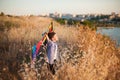 Dreamy small boy with colorful kite among dry grass on sea coast with town on background