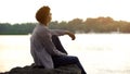 Dreamy teen sitting on river bank and thinking about sense of life, back view