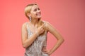 Dreamy tender attractive blond young woman in stylish silver shiny dress pointing looking upper right corner amused Royalty Free Stock Photo