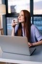 Dreamy thinking young woman using laptop computer and drinking coffee at home workplace. Royalty Free Stock Photo