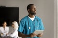 Dreamy thoughtful handsome African American doctor holding digital tablet Royalty Free Stock Photo