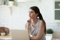 Dreamy thoughtful woman sitting at table with laptop in kitchen Royalty Free Stock Photo