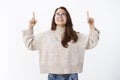 Dreamy thrilled and happy young brunette female student in glasses and sweater raising head and hands pointing, looking