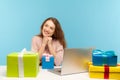 Dreamy woman office employee sitting at workplace, smiling friendly surrounded by many gift boxes and thinking