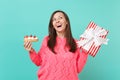 Dreamy woman in pink sweater looking up, hold eclair cake, red striped present box with gift ribbon isolated on blue Royalty Free Stock Photo