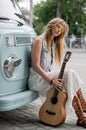 Dreamy woman sits by the camper. A hippie girl holding a guitar and leaning on a classic travel van.