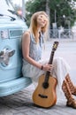 Dreamy woman sits by the camper. A hippie girl holding a guitar and leaning on a classic travel van.