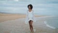 Dreamy woman walking coastline in white outfit. Thoughtful curly girl going sand Royalty Free Stock Photo