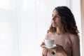 Dreamy young beautiful woman standing near window with cup of tea. Royalty Free Stock Photo