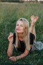 Dreamy young blond woman lying on a grass in a field, smelling wild flower Royalty Free Stock Photo