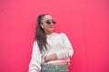 Dreamy young fashion girl wearing earphone, stylish sunglasses looking forward on pink wall background with copy space Royalty Free Stock Photo