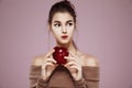 Dreamy young girl holding red apple looking in side over pink background. Royalty Free Stock Photo