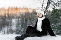 Dreamy young girl is siting on snow in winter sunny evening forest and is looking up. Royalty Free Stock Photo