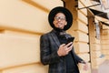 Dreamy young man wears stylish black suit looking away while standing on the street with cup of tea. Busy african guy