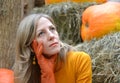 A dreamy young woman hugs her face with her hand in an orange glove. Portrait against the background of pumpkin and hay Royalty Free Stock Photo