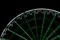 Detail view of an illuminated green and white ferris wheel and cabins in black night