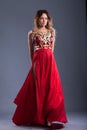 Girl in a red long dress in the studio, on a gray background.