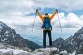 Dressed bright orange jacket backpacker man with raised armswith trekking poles enjoying the mountain valley view during mountain