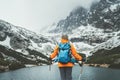 Dressed bright orange jacket female backpacker with trekking poles enjoying the Velicke pleso mountain lake view during mountain