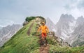 Dressed bright orange soft shell jacket backpacker running  by green mountain path with picturesque Dolomite Alps range background Royalty Free Stock Photo