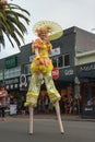 An ornately dressed female stilt walker with an umbrella