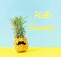 Dressed up cheerful pineapple with a black mustache and the phrase hello summer a blue yellow background. Glitch effect.