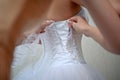 Dressing bride on wedding day. Bridesmaids lace bride. Woman holds a ribbon from brides dress