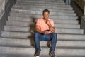 Young black man sitting on stairs inside office building, texting on cell phone Royalty Free Stock Photo