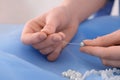 Dressmaker stringing bead on thread at light blue fabric in atelier, closeup