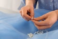 Dressmaker stringing bead on thread at light blue fabric in atelier, closeup